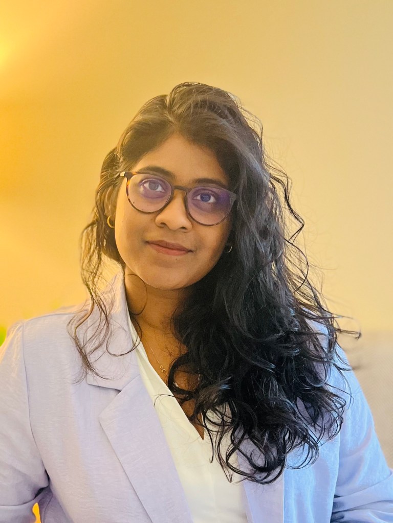 Name: Lakshana of Indian ethnicity. Brown skin female. Wearing specs. Long black hair pushed to the left side of her shoulder.